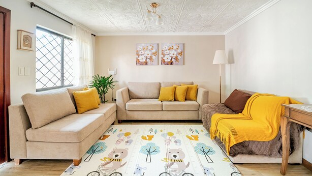 A living room with a sofa set, a coffee table, and a side table with a lamp. There is a window with curtains, a plant, and two wall-mounted paintings. - Romito | Accommodations for 5 people with parking, 5 minutes from Mall del Alto and 12 minutes from the Historic Center (Cuenca)