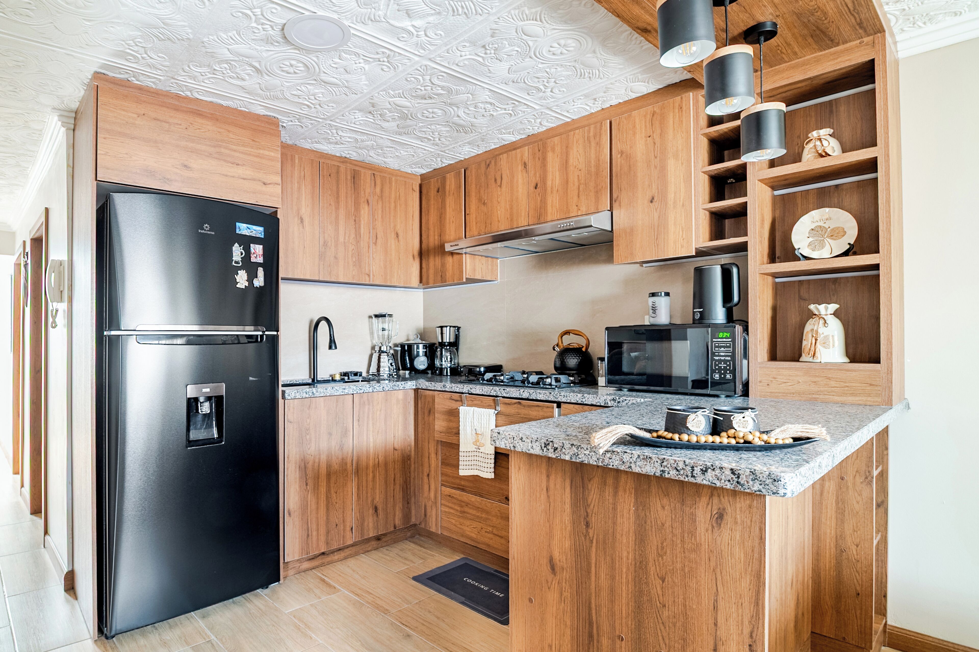 Una cocina moderna con armarios de madera, un refrigerador negro, un microondas y una cafetera.