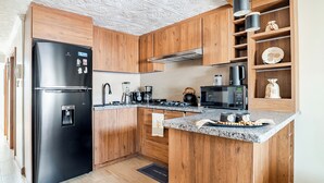 A modern kitchen with wooden cabinets, a black refrigerator, a microwave, and a coffee maker. - Romito | Accommodations for 5 people with parking, 5 minutes from Mall del Alto and 12 minutes from the Historic Center (Cuenca)