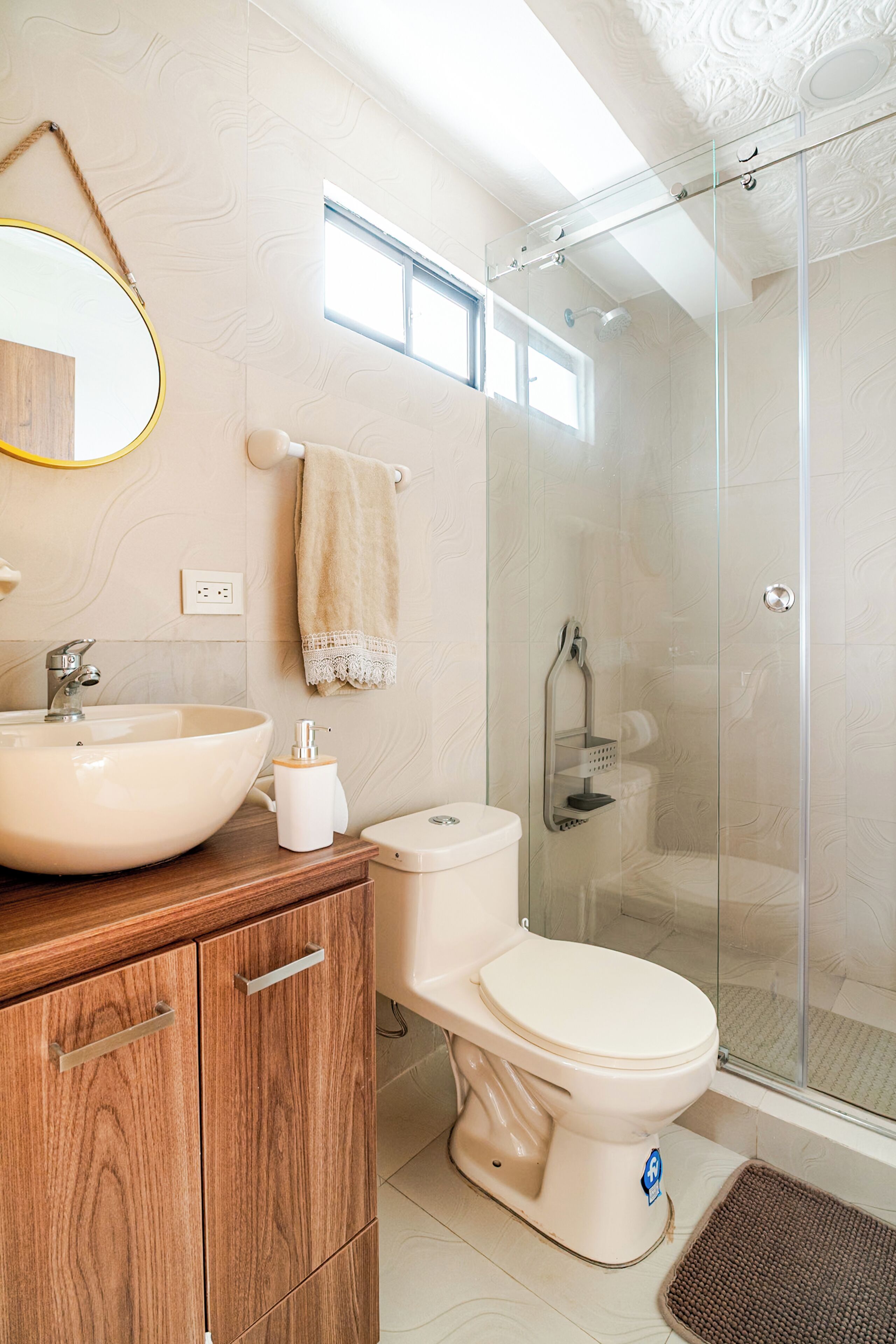 A modern bathroom with a wooden vanity, a white sink, a toilet, and a glass-enclosed shower.