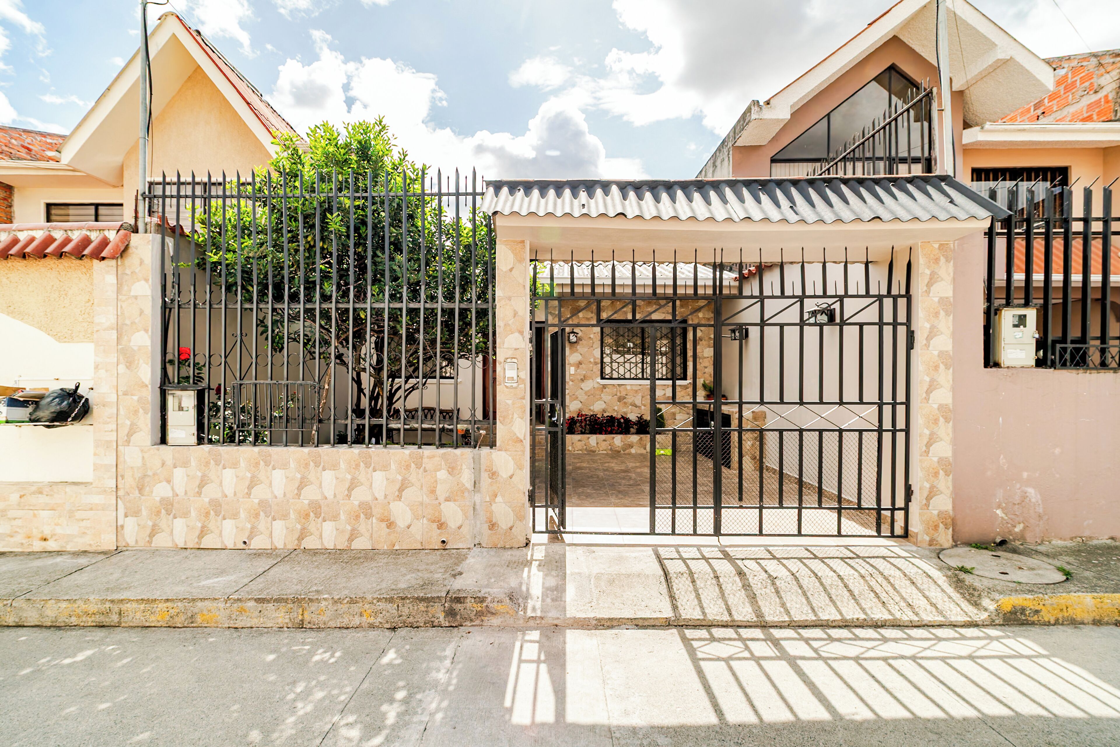 Una entrada cerrada a una propiedad residencial con techo de tejas, muro de piedra y portón metálico.