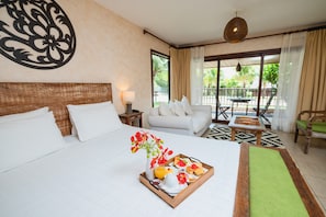 A hotel room with a bed, a dining table with breakfast, a sofa, and a view of the outdoors.