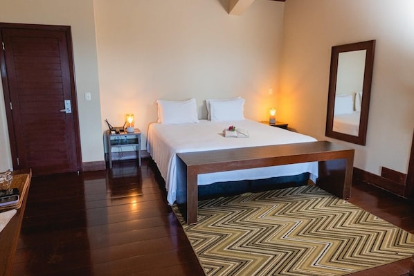 A hotel room with a bed, bedside tables, a nightstand, a mirror, and a patterned rug.