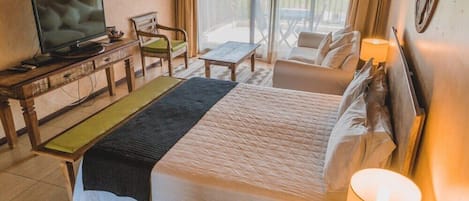 Quarto de hotel com cama, televisão, escrivaninha e varanda com área de estar.