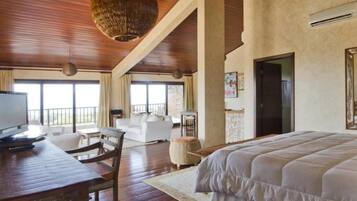 Quarto de hotel com uma cama grande, uma escrivaninha com cadeira, televisão e varanda com vista.