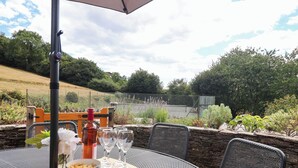 An outdoor dining area with a round metal table, chairs, a bottle of red wine, wine glasses, a bowl of lemons, and a wooden bench. - IRIS AT STANCOMBE MANOR, pet friendly, with pool in Chillington (Kingsbridge)