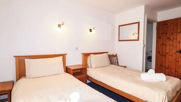 Habitación de hotel con dos camas, cabeceros de madera, mesitas de noche, un espejo y un armario de madera.