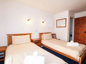 Een hotelkamer met twee bedden, houten hoofdeinden, nachtkastjes, een spiegel en een houten garderobe.