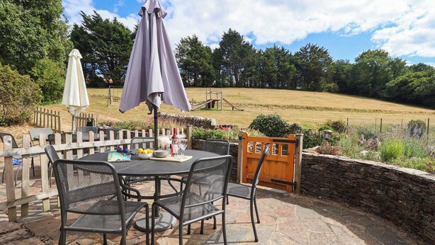 An outdoor patio with a round table, chairs, and a wooden fence. - IRIS AT STANCOMBE MANOR, pet friendly, with pool in Chillington (Kingsbridge)