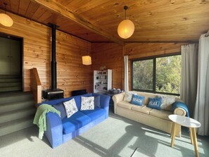 A cozy cabin interior with a blue sofa, beige sofa, and a small table. - Hekerua Bay Views (Waiheke Island)