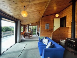 A wooden interior with a sofa, a fireplace, and a dining area. - Hekerua Bay Views (Waiheke Island)