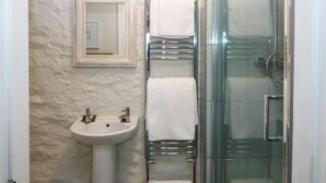 Un baño con cabina de ducha de vidrio, un lavabo blanco y un perchero con toallas blancas.