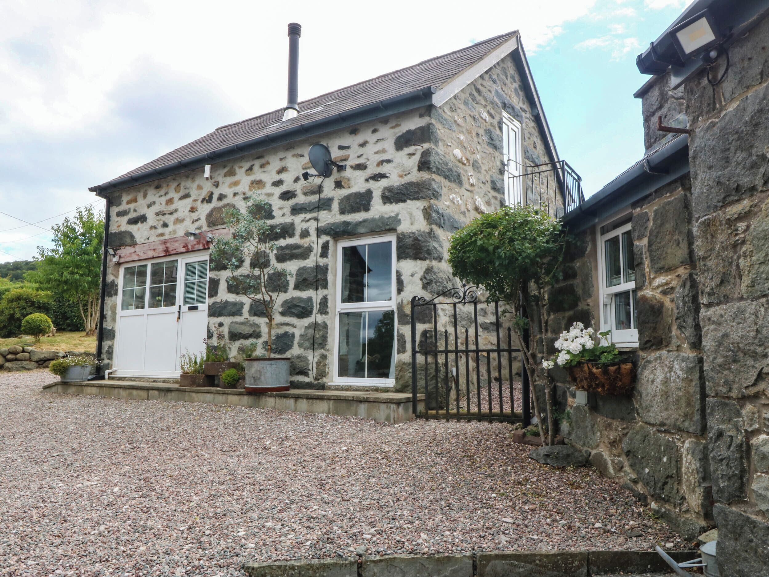 A stone building with a gravel driveway, a white door, and a small garden area.