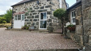 Un edificio de piedra con camino de grava, una puerta blanca y un pequeño jardín.
