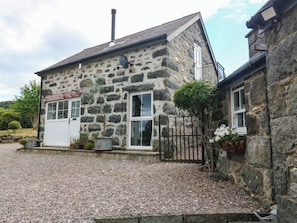 A stone building with a gravel driveway, a white door, and a small garden area. - LITTLE OAK, pet friendly, character holiday cottage in Tal-Y-Bont (Conwy)