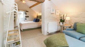 Un dormitorio acogedor con cama, cómoda, radiador, sillón colgante, mesita con lámpara y sofá azul.