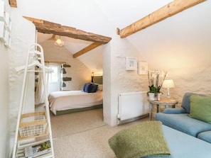A cozy bedroom with a bed, a dresser, a radiator, a hanging chair, a small table with a lamp, and a blue sofa. - LITTLE OAK, pet friendly, character holiday cottage in Tal-Y-Bont (Conwy)