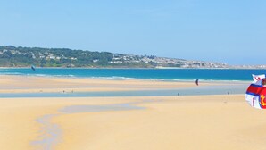 A beach with a clear sky, a flag, and a distant town. - TOP DECK, pet friendly, character holiday cottage in St Ives (St. Ives)