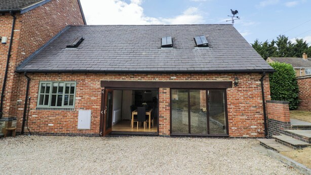 A brick building with a sloped roof, a large sliding glass door entrance, and a gravel driveway. - UNDERHILL HOUSE ANNEX, pet friendly in Stratford-Upon-Avon (Stratford-upon-Avon)