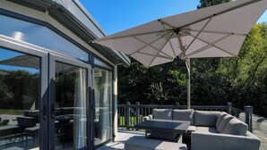 Eine überdachte Terrasse im Freien mit Sitzgelegenheit, darunter ein Sofa und ein Tisch, und ein großer Sonnenschirm, der Schatten spendet.