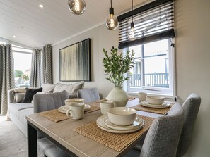 A modern living room with a dining table set for four, a sofa, a large abstract painting, and a window with blinds.