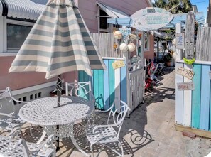 A patio area with a striped umbrella, a round metal table, and white metal chairs.