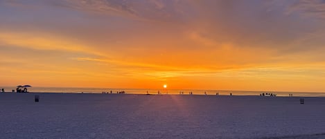 A beach at sunset with a clear sky and the sun near the horizon.