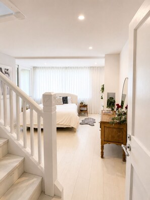 Um quarto com cama, mesa de cabeceira, penteadeira, espelho, escada e janela com cortinas.