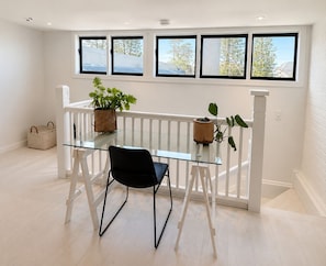Quarto com mesa de vidro, duas cadeiras, um vaso de plantas e vista pelas janelas.
