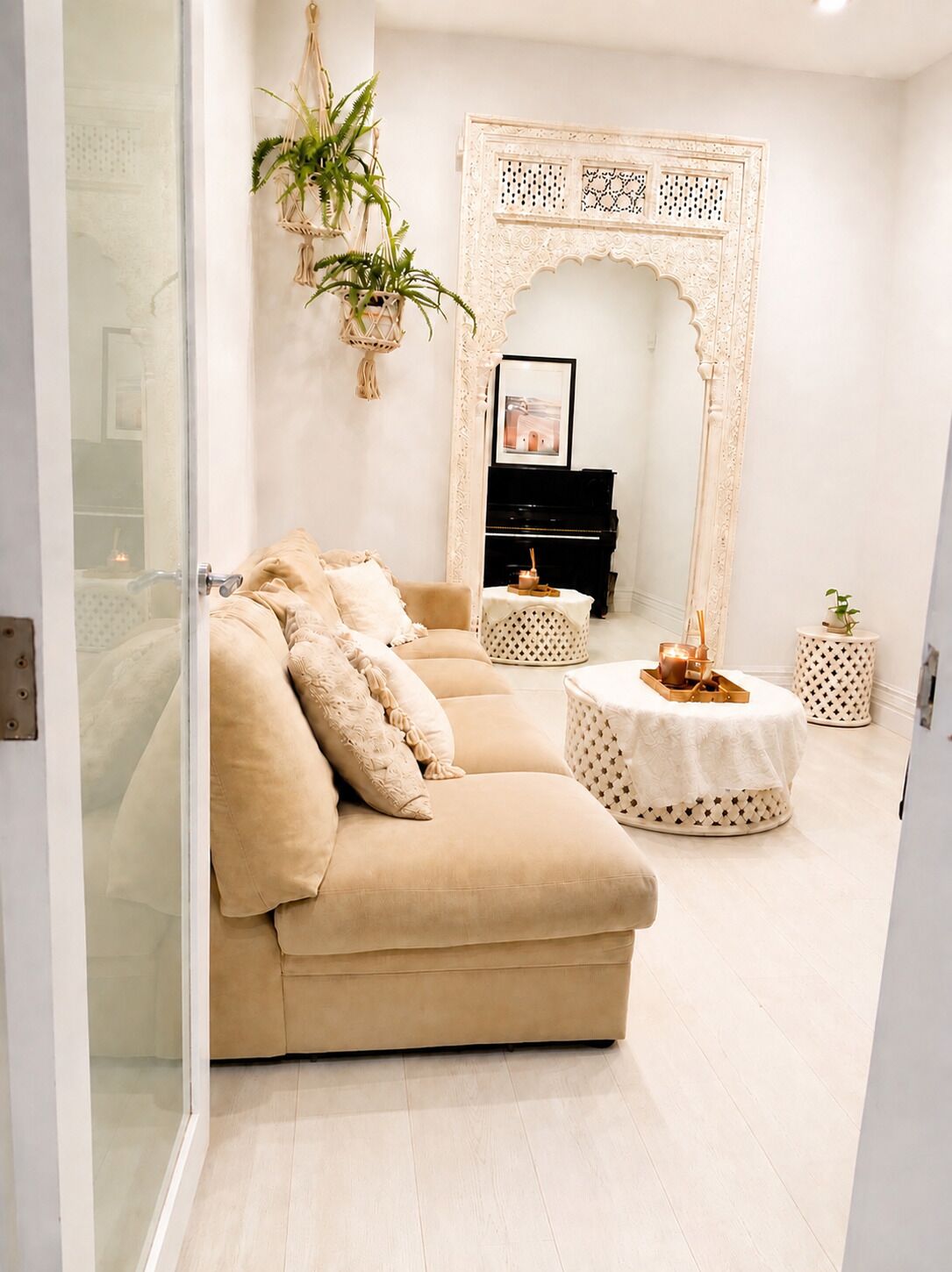 A living room with a beige sofa, a round coffee table, a piano, and a decorative archway.