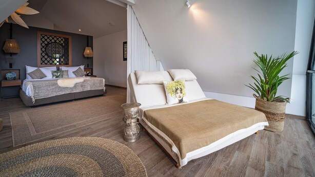 A modern bedroom with a large bed, a smaller sofa, and a potted plant.