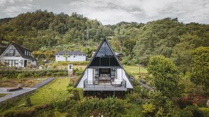 A modern house with a triangular roof, surrounded by lush greenery and hills.