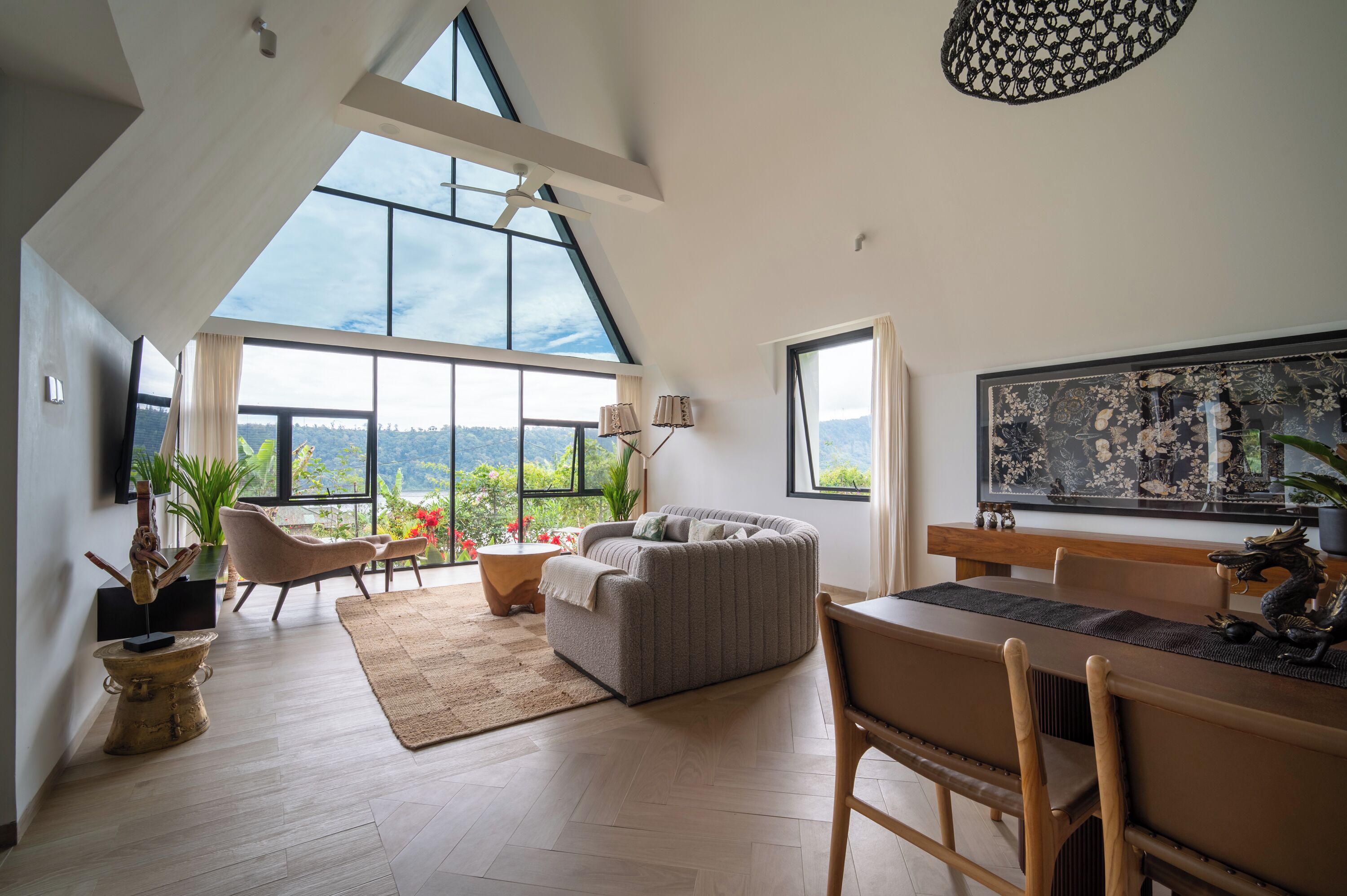 A spacious living area with a large window, a sofa, a dining table, and a ceiling fan.