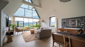 A spacious living area with a large window, a sofa, a dining table, and a ceiling fan.