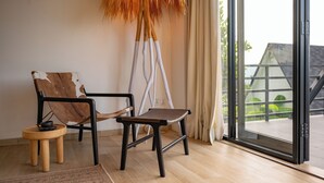 A modern interior with a wooden floor, a leather chair, a small wooden stool, and a large window with a view of a building outside.