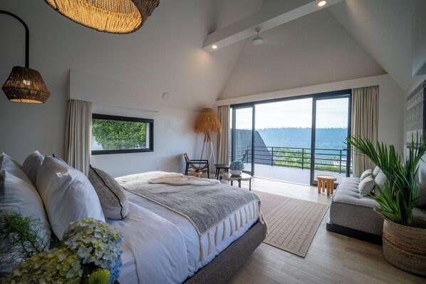 A bedroom with a large bed, a balcony with a view, and a dining area with a table and chairs.