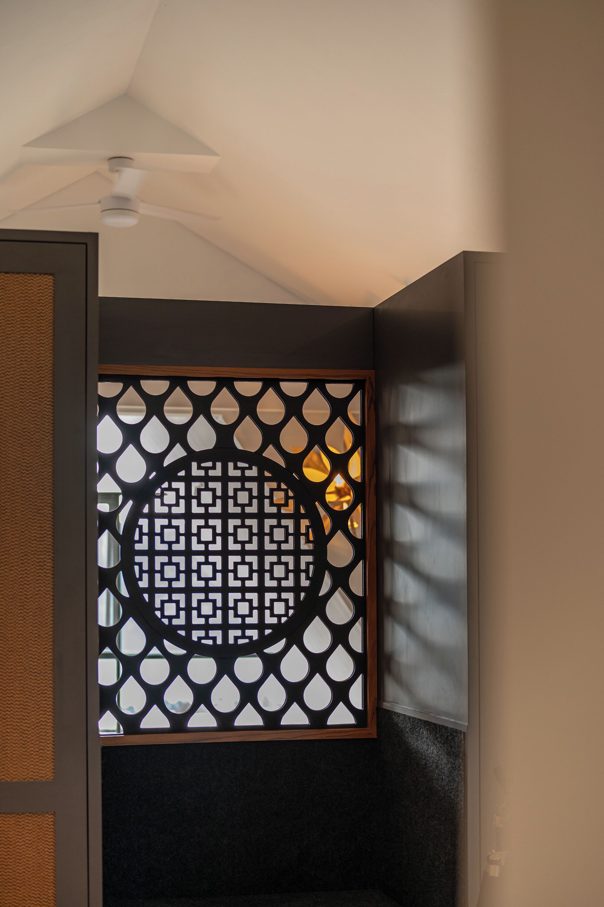A room with a ceiling fan, a black and white patterned partition, and a view of the outside.