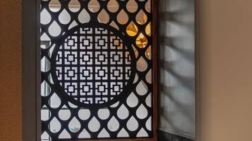 A room with a ceiling fan, a black and white patterned partition, and a view of the outside.
