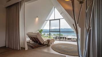 A room with a large window, a lounge chair, a small table, and a view of a body of water.