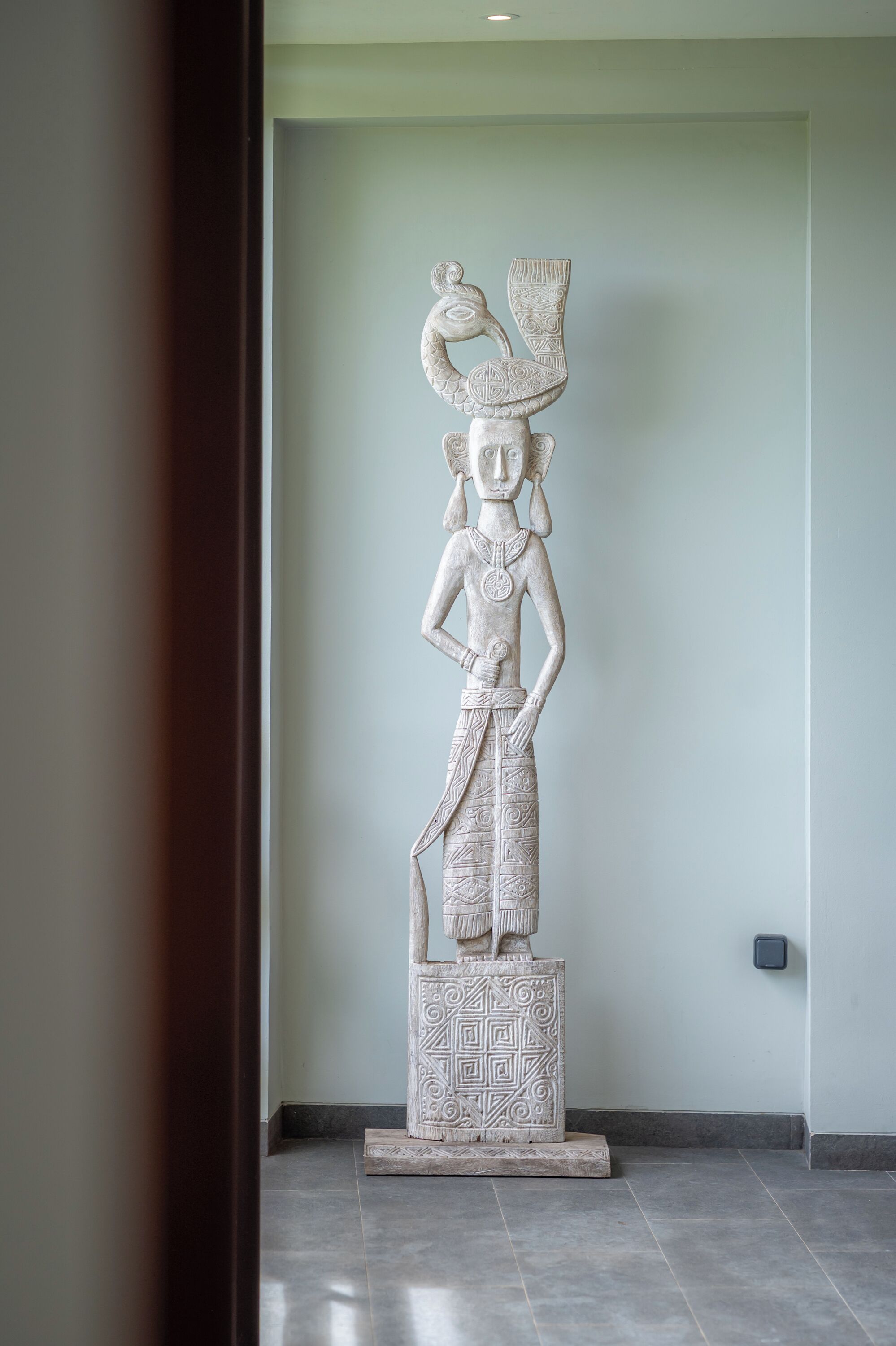 A white statue of a figure with a headdress, standing on a pedestal with geometric patterns.