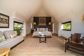 A spacious room with a large bed, a sofa, and a coffee table. There are two windows providing natural light.
