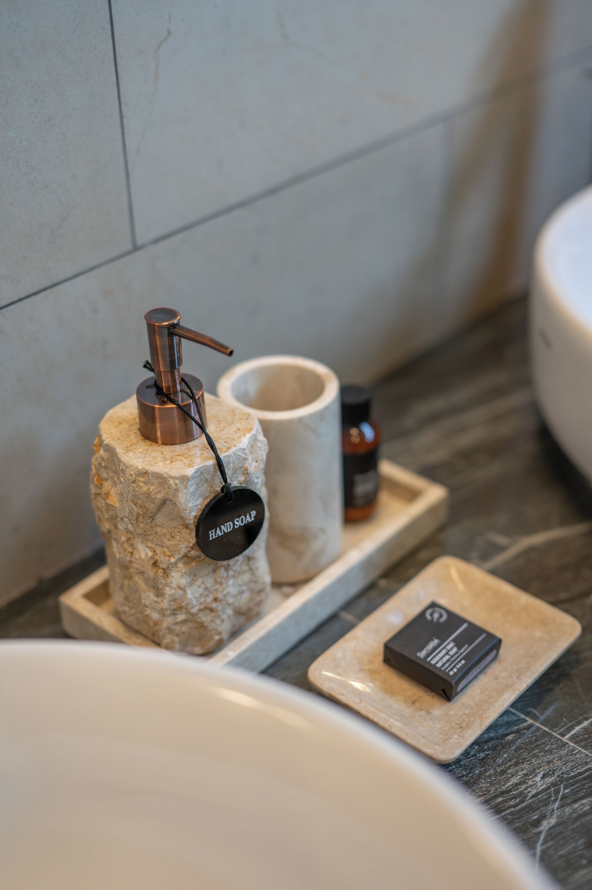 Une salle de bain avec un distributeur de savon liquide posé sur une pierre, un pain de savon et un flacon de savon sur un plateau.