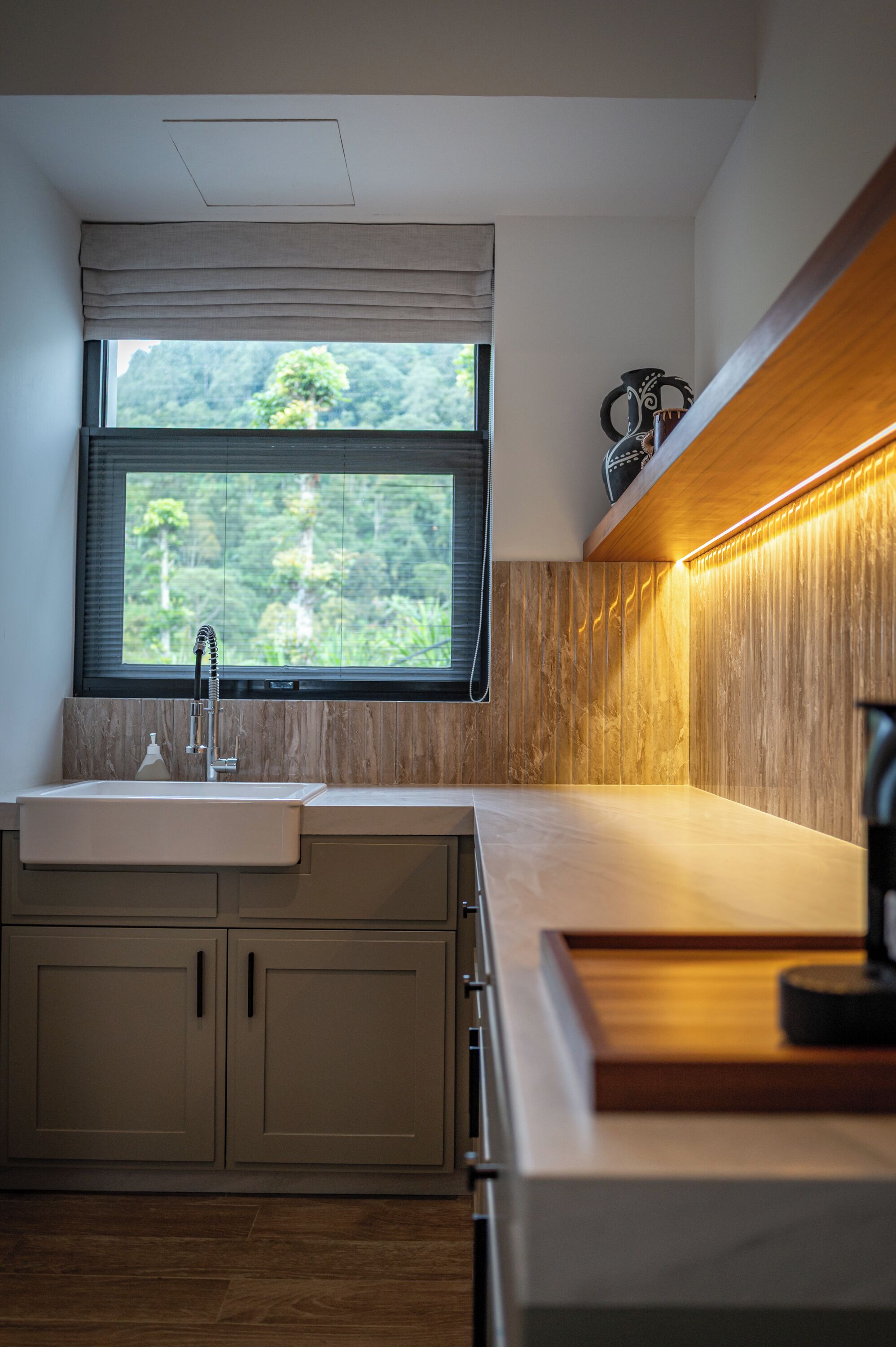 A modern kitchen with a built-in sink, wooden cabinets, a window with a view of greenery, and a countertop with a light fixture.