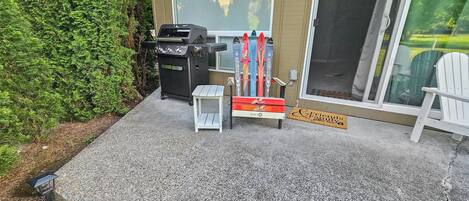 Un patio con una parrilla, una mesita, un felpudo y una silla blanca.