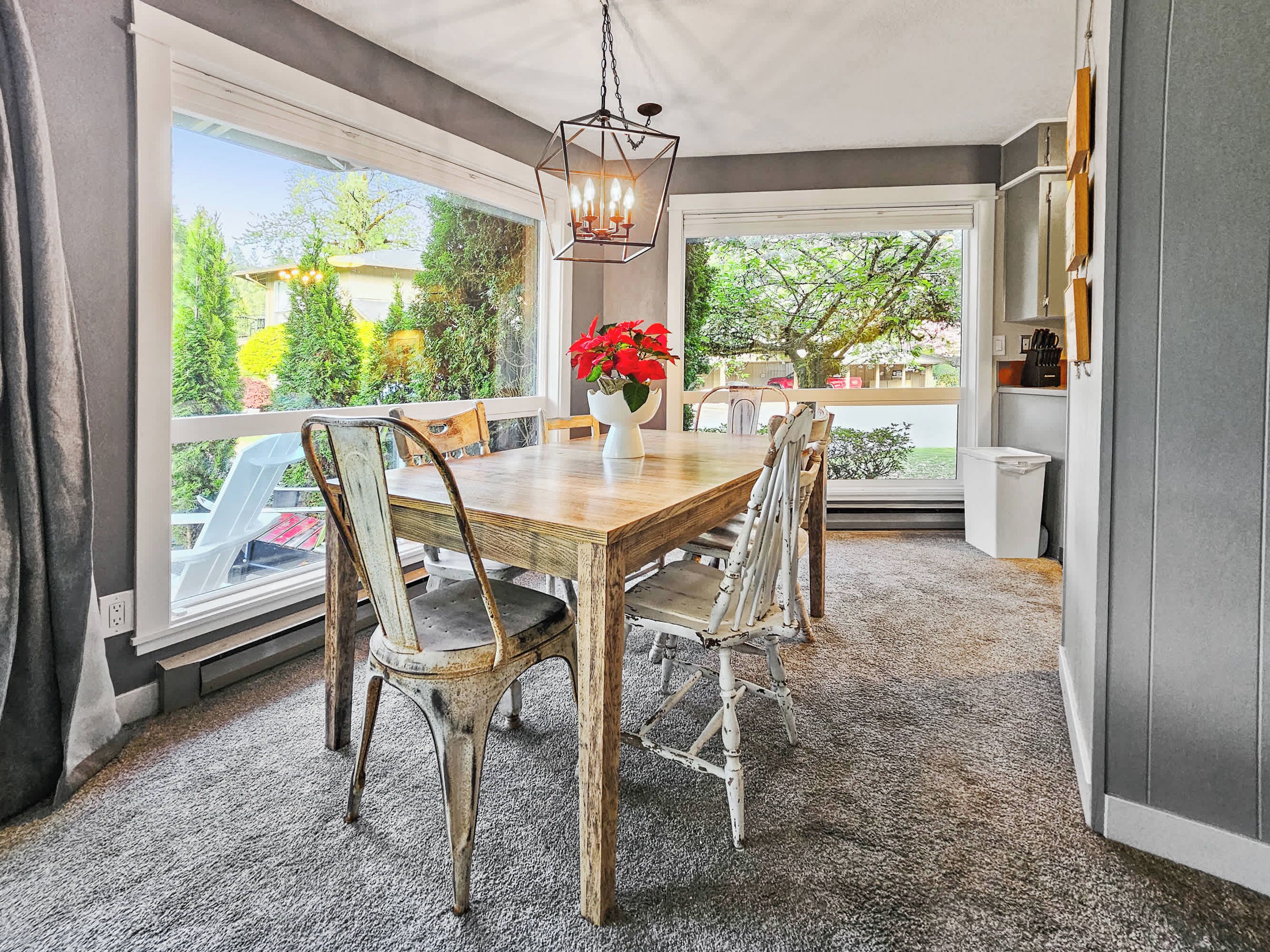 Un espace repas comprenant une table et des chaises en bois, un luminaire suspendu et une vue dégagée sur l’extérieur grâce à de grandes fenêtres.