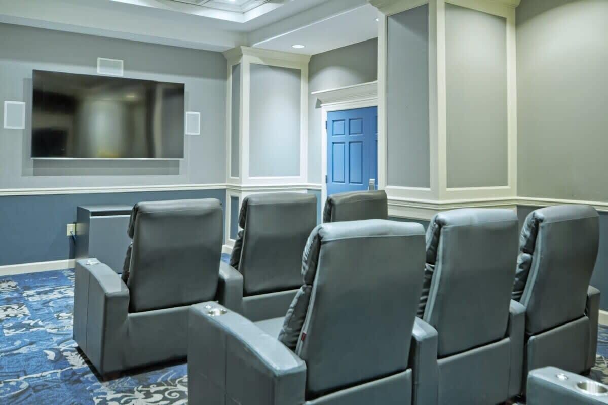 A conference room with grey leather chairs, a large flat-screen TV, and a blue door.