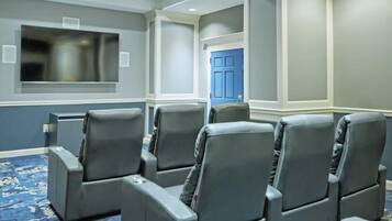 A conference room with grey leather chairs, a large flat-screen TV, and a blue door.