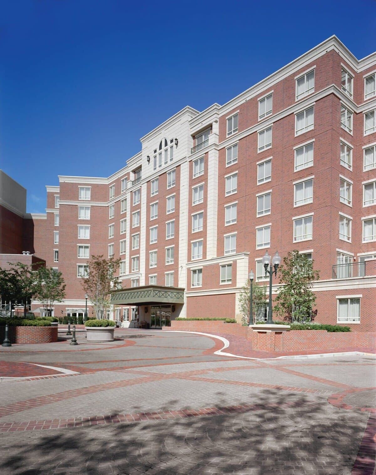 A multi-story hotel with a brick facade, large windows, and a central courtyard with a covered seating area.