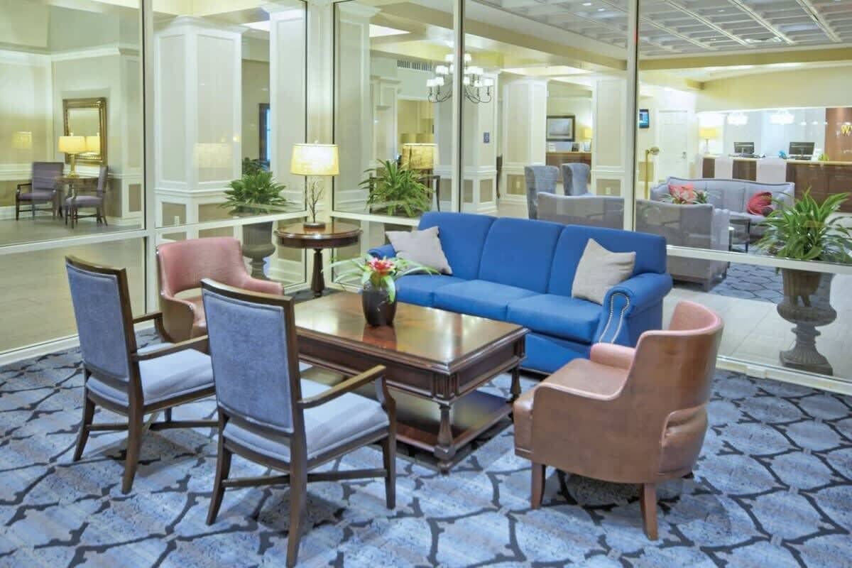 A lobby with a blue sofa, two armchairs, a coffee table, and a mirror reflecting the room.