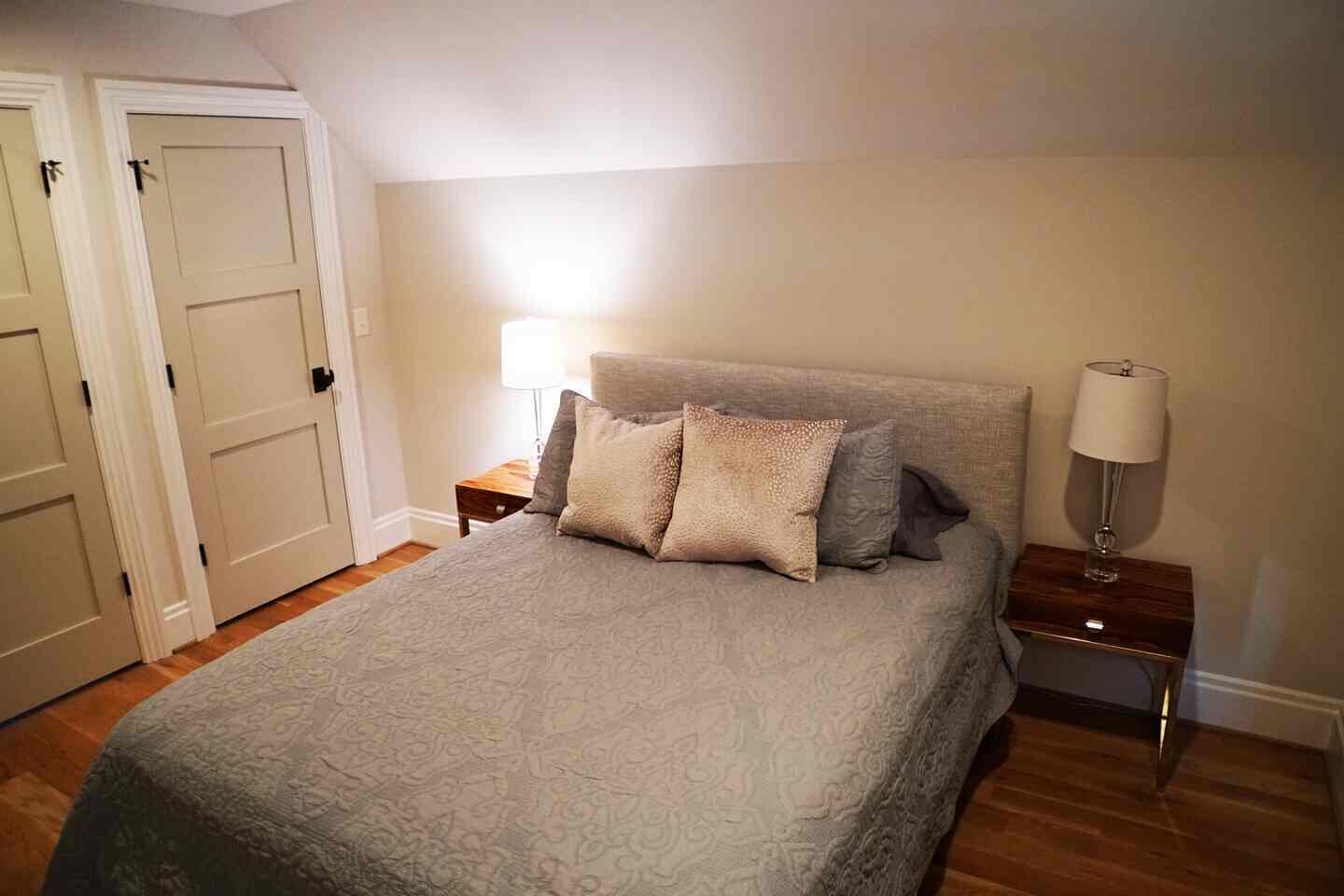 Un dormitorio con una cama, dos mesitas de noche, una lámpara y una puerta.